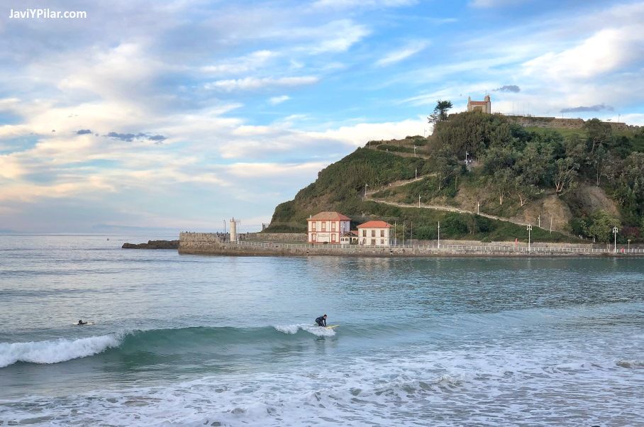 Surfista en la playa de Santa Marina en Ribadesella (Asturias, España) con la ermita de La Guía al fondo